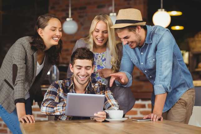 Laughing friends looking at tablet at coffee shop