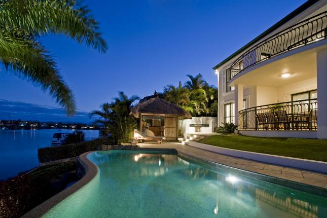 Luxurious mansion exterior at dusk overlooking pool, canal and Bali hut